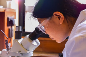 Female student wearing safety goggles looking into a microscope